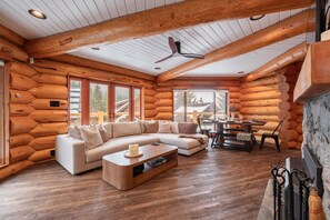 A log cabin interior with a large L-shaped sofa, a dining table, and a fireplace. - Luxury log chalet | Private hot tub | Ski-in/out (Whistler)