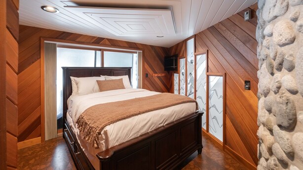 Een slaapkamer met een houten schuine plafond, een groot bed met hoofdeinde, en een stenen muur.