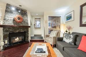 A living room with a fireplace, a couch, a coffee table with remotes, and a door with a window. - Excellent location | Private hot tub | Pets | BBQ (Whistler)