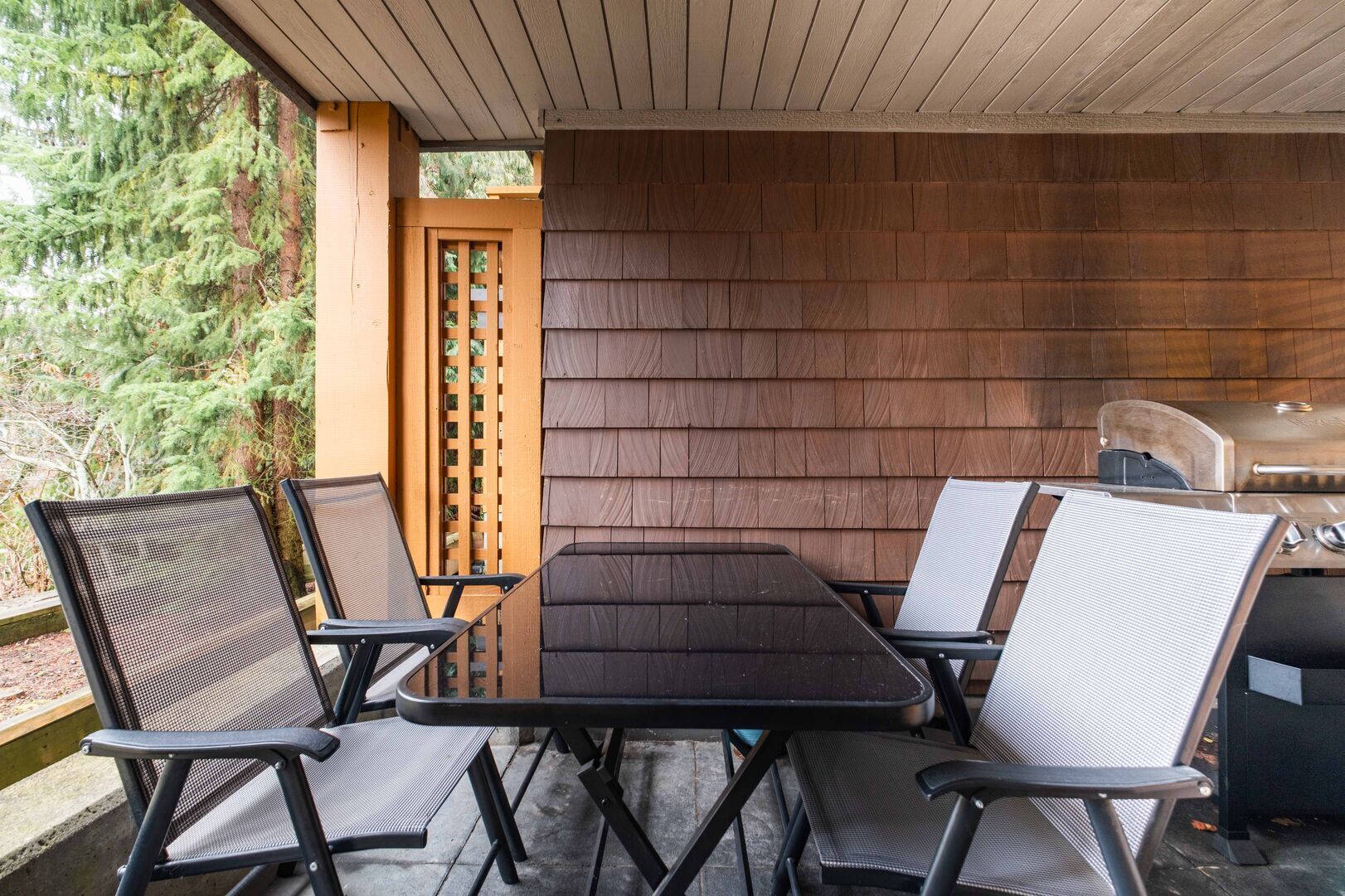 Un patio al aire libre con una mesa, sillas, una parrilla y una valla de madera.