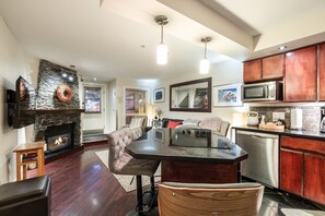 A modern kitchen with a stone fireplace, wooden cabinets, and a dining area with a glass-top table. - Excellent location | Private hot tub | Pets | BBQ (Whistler)