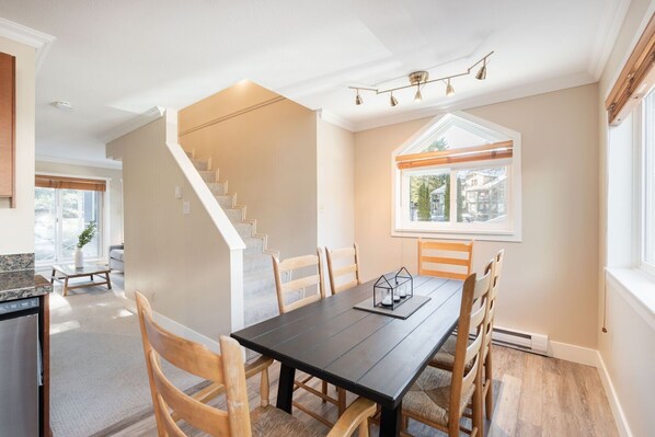 A dining area with a dark wooden table, six wooden chairs, a staircase, and a window with blinds. - Private Bike Storage | Free parking | Mountain Views | Window AC (Whistler)