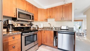 A modern kitchen with wooden cabinets, stainless steel appliances, and a granite countertop. - Private Bike Storage | Free parking | Mountain Views | Window AC (Whistler)