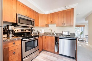 A modern kitchen with wooden cabinets, stainless steel appliances, and a granite countertop. - Private Bike Storage | Free parking | Mountain Views | Window AC (Whistler)
