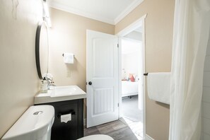 Une salle de bain comprenant des toilettes, un lavabo, un miroir et une porte donnant sur une chambre.