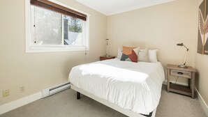 A bedroom with a large bed, a window with blinds, bedside tables with lamps, and a wall-mounted artwork. - Private Bike Storage | Free parking | Mountain Views | Window AC (Whistler)