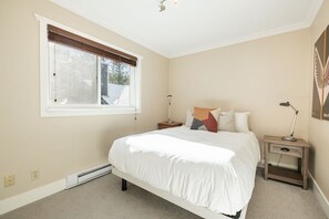 A bedroom with a large bed, a window with blinds, bedside tables with lamps, and a wall-mounted artwork. - Private Bike Storage | Free parking | Mountain Views | Window AC (Whistler)