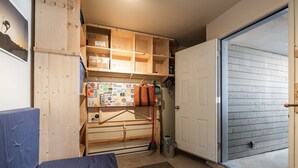 A compact storage area with wooden shelves, a metal rack, and a door leading to an outdoor area. - Private Bike Storage | Free parking | Mountain Views | Window AC (Whistler)