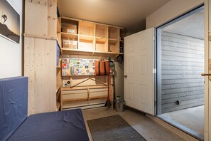 A compact storage area with wooden shelves, a metal rack, and a door leading to an outdoor area. - Private Bike Storage | Free parking | Mountain Views | Window AC (Whistler)
