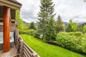 A well-maintained garden with a wooden deck, a hot tub, and a view of a mountain range. - Spacious townhome | Private garage & hot tub | BBQ (Whistler)