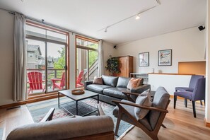 A modern living room with a sofa, chairs, a coffee table, and a view of the outdoors. - Spacious townhome | Private garage & hot tub | BBQ (Whistler)
