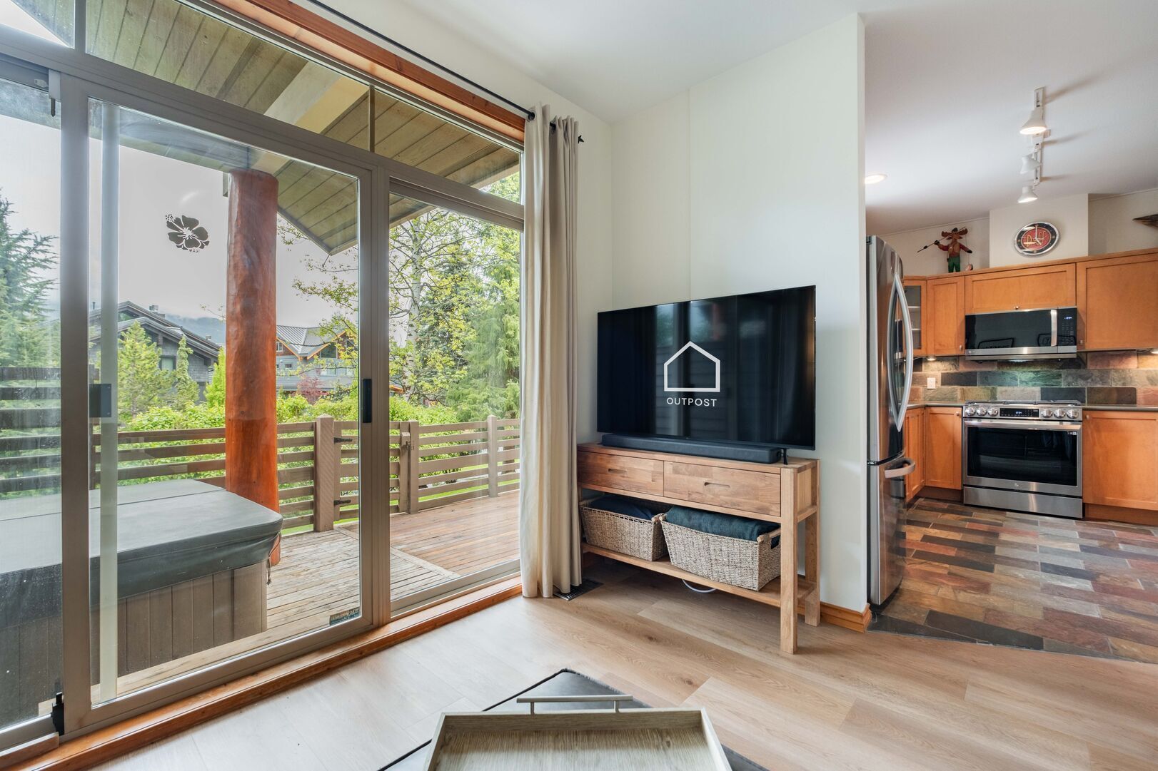A modern kitchen with a flat-screen TV, wooden cabinets, and a stone-patterned floor.