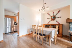A dining area with a table and chairs, a chandelier, and a wall with a decorative piece. - Spacious townhome | Private garage & hot tub | BBQ (Whistler)