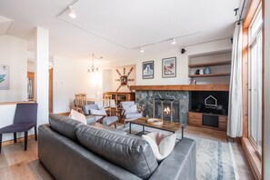 Ein modernes Wohnzimmer mit Kamin, Sitzgruppe und einem Fernseher mit der Aufschrift 'OUTPOST'.