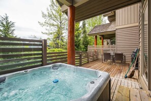 A hot tub on a wooden deck with a view of a house and trees. - Spacious townhome | Private garage & hot tub | BBQ (Whistler)