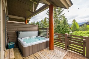 Ein Whirlpool auf einer Holzterrasse mit Holzzaun und Bäumen im Hintergrund.
