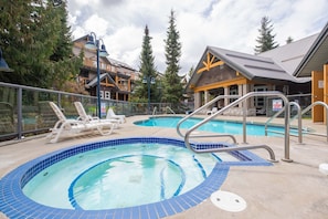 A swimming pool area with lounge chairs, a lifeguard station, and a building with a yellow accent. - Private hot tub | Pets | BBQ | Location! (Whistler)