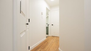 Un estrecho pasillo con paredes blancas y piso de madera, que conduce a una puerta. Se ve un armario verde al fondo.