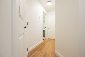 Ein schmaler Flur mit weißen Wänden und Holzboden, der zu einer Tür führt, im Hintergrund ist ein grüner Schrank zu sehen.