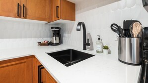 Cocina con armarios de madera, un grifo negro, una cafetera, dispensador de jabón y un portalapices.
