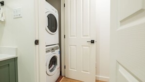 Un lavadero con dos lavadoras apiladas y una puerta que da a otra habitación.