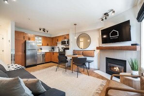 Un salon moderne avec un canapé, un coin repas avec des chaises, une cuisine avec des meubles en bois, un téléviseur à écran plat et une cheminée.