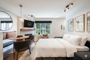 A modern hotel room with a bed, a sofa, a dining table, and a TV. - Private hot tub | Pets | BBQ | Location! (Whistler)