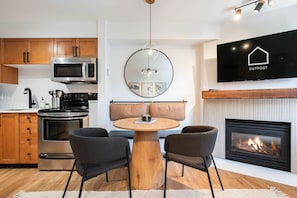 A modern kitchen with a dining area, a flat-screen TV, and a fireplace. - Private hot tub | Pets | BBQ | Location! (Whistler)
