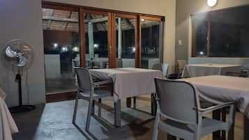 Zona pranzo con tavoli e sedie, una ventola e vista attraverso una porta in vetro.