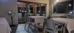 A dining area with tables and chairs, a fan, and a view through a glass door.