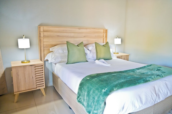 A neatly made bed with a green throw blanket, two bedside lamps, and a wooden headboard.