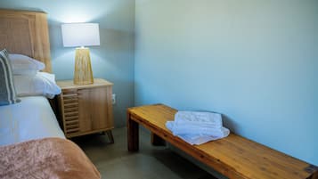 Habitación de hotel con cama, mesita de noche con lámpara, banco de madera y enchufe en la pared.