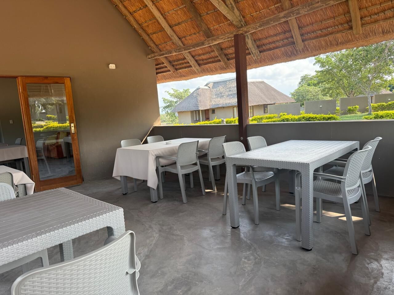 An outdoor patio with tables and chairs, a wooden ceiling, and a view of buildings in the background.