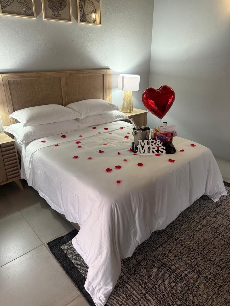 A neatly made bed with white linens, a heart-shaped balloon, and a 'MR & MRS' sign on a hotel room.