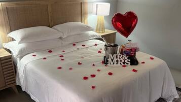 A neatly made bed with white linens, a heart-shaped balloon, and a 'MR & MRS' sign on a hotel room.