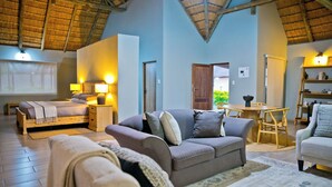 A spacious living area with a high ceiling, a sofa set, a bed, and a dining table.