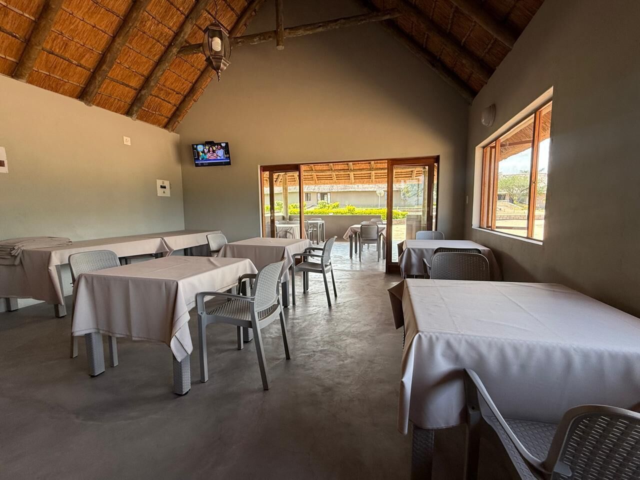 A dining area with tables and chairs, a television on the wall, and a view of the outdoors.