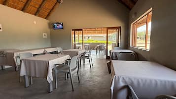A dining area with tables and chairs, a television on the wall, and a view of the outdoors.