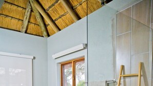 A bathroom with a freestanding bathtub, a glass shower enclosure, a wooden ladder, and a window with a view of greenery.