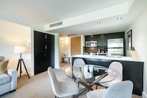 A modern kitchen with a central island, a dining area with a glass table and chairs, and a sofa in a living area. - Stunning ski-in/out | AC | Complex pool & hot tub (Whistler)