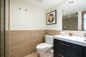 A bathroom with a toilet, a sink with toiletries, a mirror, and a framed artwork on the wall. - Stunning ski-in/out | AC | Complex pool & hot tub (Whistler)