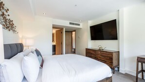 Una habitación de hotel moderna con una cama grande, un aparador de madera, un televisor de pantalla plana y un adorno decorativo en la pared.