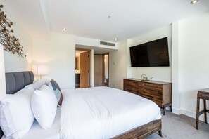 Ein modernes Hotelzimmer mit einem großen Bett, einer Holzkommode, einem Flachbildfernseher und einer dekorativen Wandgestaltung.
