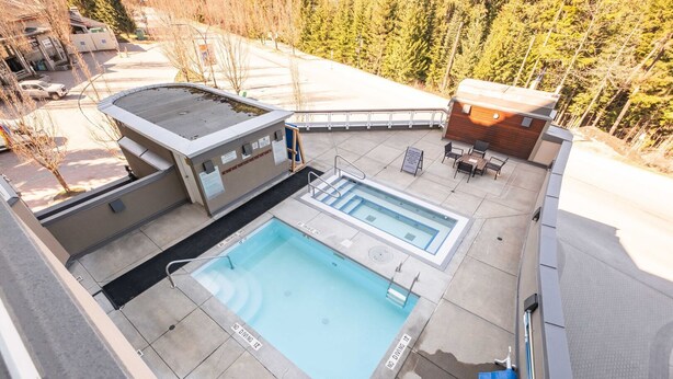 Piscina en la azotea con trampolín y sillones de descanso, rodeada de árboles.
