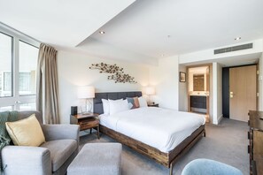 A hotel room with a large bed, a bedside table, a lamp, a chair, and a view of the city. - Stunning ski-in/out | AC | Complex pool & hot tub (Whistler)