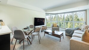 Una sala de estar moderna con un ventanal grande, un televisor de pantalla plana, una zona de comedor con sillas y un sofá.