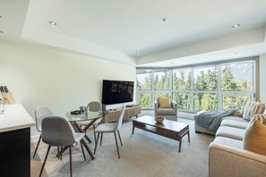 Ein modernes Wohnzimmer mit großem Fenster, einem Flachbildfernseher, einem Essbereich mit Stühlen und einem Sofa.