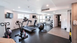 Un gimnasio moderno con diversos equipos de ejercicio, ventanas amplias y un interior limpio y bien iluminado.