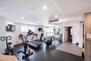 Ein modernes Fitnessstudio mit verschiedenen Trainingsgeräten, großen Fenstern und einem sauberen, hellen Innenraum.