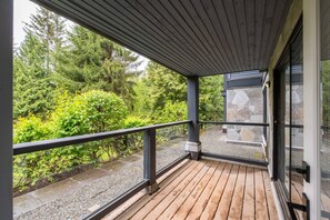 A wooden deck with a glass railing overlooking a garden with various plants and trees. - Walk to Blackcomb | Complex hot tub | BBQ (Whistler)